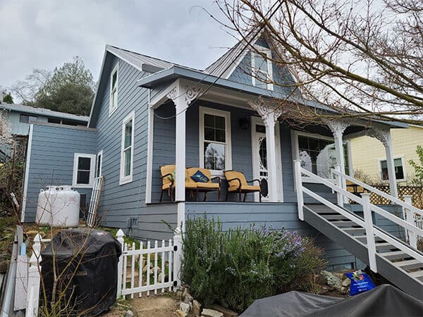 Blue cottage with horizontal siding and decorative white porch trim
