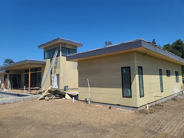 Single-story addition under construction with large windows and panel siding