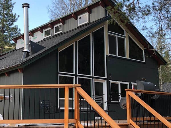 Dark cabin with vertical panel siding, white trim, and large windows
