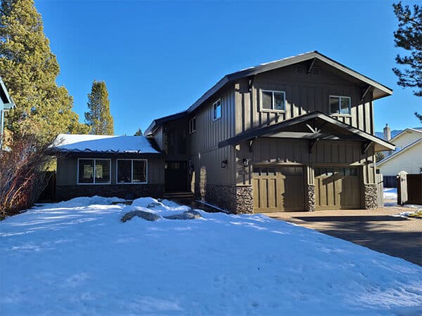Dark brown mountain home with vertical siding and timber accents in snow