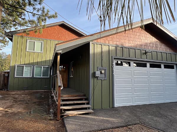 Green two-story home with vertical siding and red shingle gable