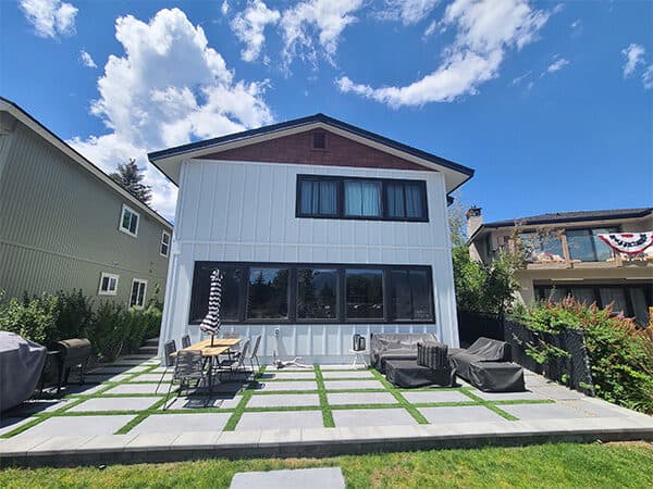 White two-story home with vertical siding, black windows, and modern patio